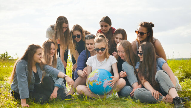 A group of cheerful girls is exploring the globe of the world in the meadow.