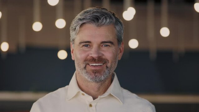 Successful aged man in formal outfit turning head and looking at camera while standing at the office building. Bearded caucasian person posing at office center.