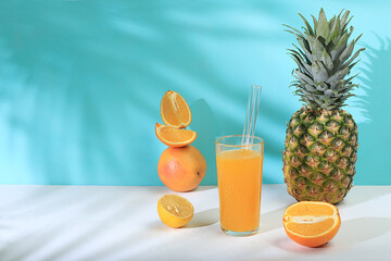 Modern still life with citrus fruits, orange juice and pineapple on azure background with long hard shadows, minimal detox diet concept, summer vitamin drinks, selective focus