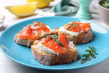 Delicious sandwiches with cream cheese, salmon and arugula on light blue plate, closeup