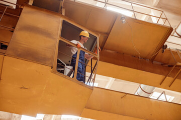 Cheerful builder standing in operator cabin of overhead crane