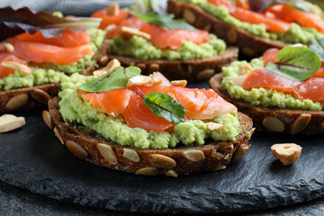 Delicious sandwiches with salmon, avocado and herbs on slate plate, closeup