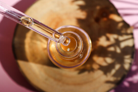 Serum oil is dripping from dropper on a wood cut close-up. Hard light with deep shadows. Selective focus. Serum skin care product. Top view, flat lay