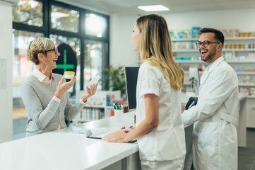 Obraz premium Two pharmacist giving prescription medications to senior female customer in a pharmacy