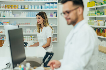 Obraz premium Happy young female pharmacist working with young male colleague in a pharmacy