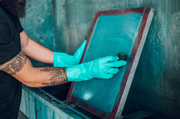 Male worker cleaning screen frame with a sponge in a printing workshop