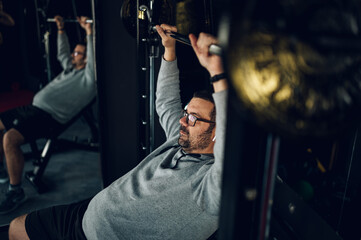 Middle aged man lifting barbell while training in the gym