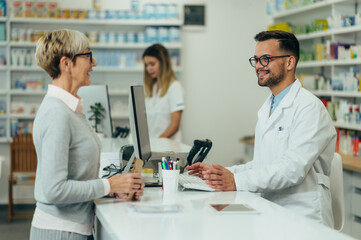 Young male pharmacist giving prescription medications to senior female customer in a pharmacy