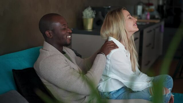 Mid adult caucasian woman getting back massage from her african american husband at home.