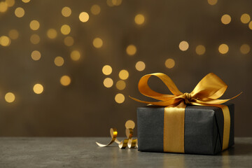 Beautifully wrapped gift box on grey table against blurred festive lights, space for text