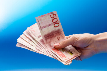 a bundle of money in a hand on a blue background. swedish kroner 500 denomination close up - obrazy, fototapety, plakaty