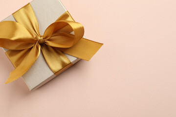 Beautiful gift box with golden bow on pink background, top view. Space for text
