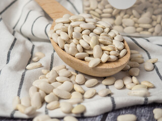 white beans in a wooden cup and spoon are scattered on the table