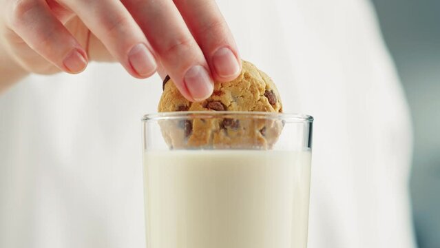 Eating cookie with milk in glass cup close-up. Glass with yogurt, dairy products concept. Drinking fresh lactose-free milk in morning.