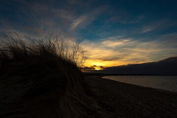 Wydmy podmyte przez fale, plaża o zachodzie słońca.