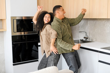 Curly woman and her guy dancing in the kitchen and singing. Merry multiracial couple having fun, fooling around while preparing dinner at home. Humor concept