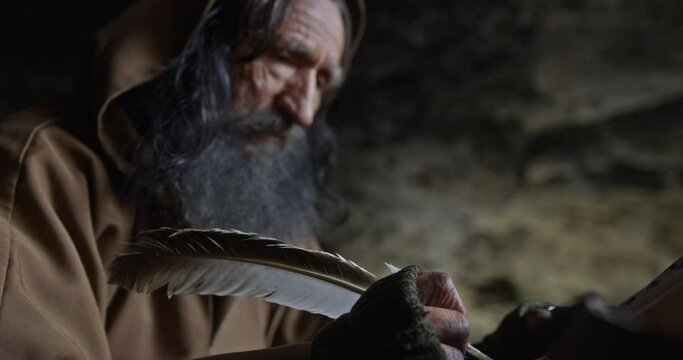 Elderly monk taking notes with quill in cave