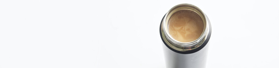 Open metal thermos or thermo mug with hot coffee and cream. White background. View from above. Free space for an inscription. Web banner. Selective focus