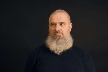 Obraz premium a man with an unshaven gray beard looks to the side on a black background, close-up