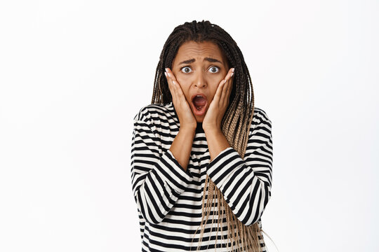 Image of shocked and terrified black woman reacting to bad concerning news, looking worried or scared, standing startled against white background