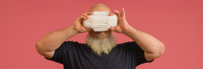 bearded man covering his face with feminine sanitary pad on pink background