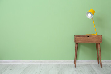 Glowing lamp on wooden table near color wall