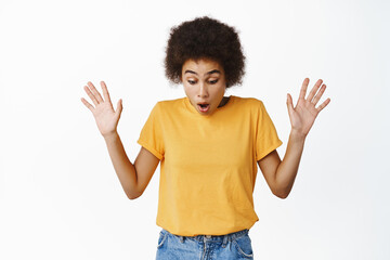 Image of african girl looking down with surprised, startled face, dropping something on floor,...