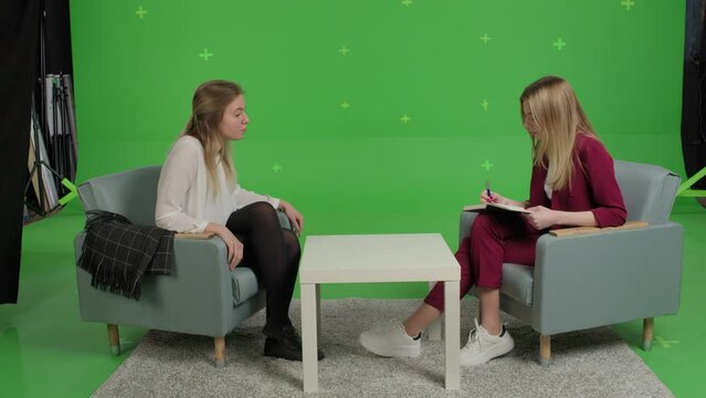 Young female patient and woman psychologist at psychotherapy session over green screen background. Youth talk show interview with a famous guest