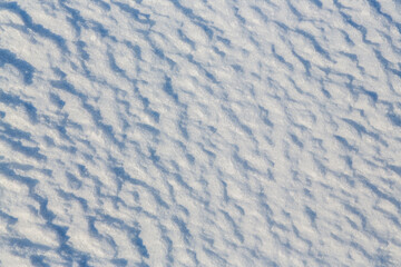 Beautiful winter background with snowy ground. Natural snow texture. Wind sculpted patterns on snow surface.