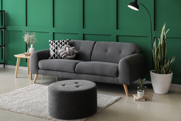 Comfortable pouf, sofa, floor lamp and houseplants near color wall - obrazy, fototapety, plakaty