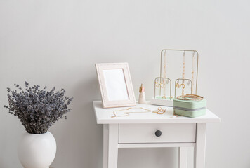 Fototapeta premium Table with stylish jewelry and vase with flowers near light wall