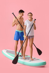 Young couple with board for sup surfing on color background