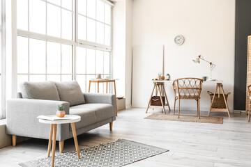 Interior of light living room with sofa, workplace and big window