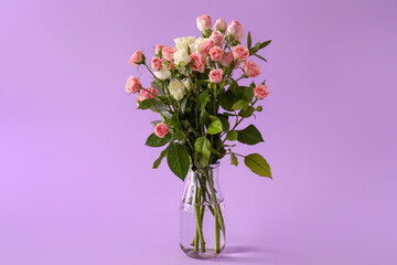 Vase with bouquet of beautiful roses on purple background