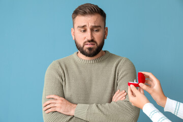 Young woman proposing to her confused boyfriend on color background