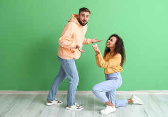 Young woman proposing to her shocked boyfriend on color background