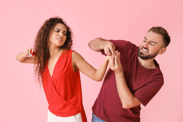 Young man trying to take engagement ring off the finger of his displeased girlfriend by force on color background