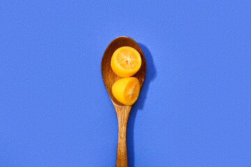 Spoon with tasty cut kumquat on blue background
