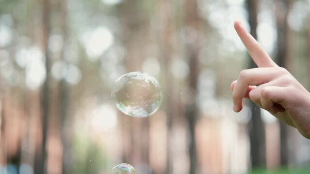 little girls finger pops a soap bubble. no face. blurred background.
