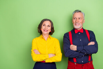 Portrait of two positive aged pensioners folded arms look interested empty space isolated on green color background