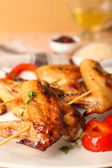 Plate with grilled chicken wings skewers on beige background, closeup