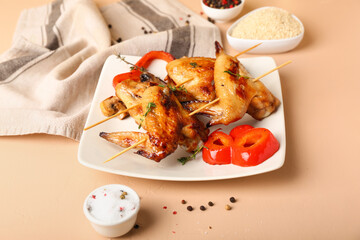 Plate with grilled chicken wings skewers on beige background