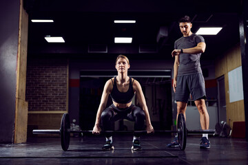 Fototapeta na wymiar A young fit sportswoman lifting barbell in gym with her coach.