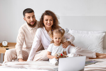 Happy young family with laptop in bedroom at home