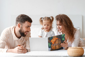 Happy young family reading book in bedroom at home