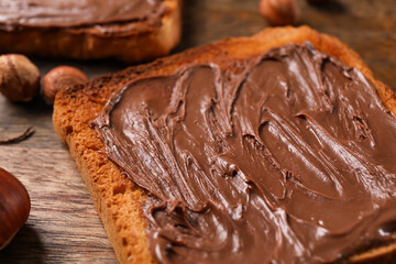 Wooden board of bread with chocolate paste and hazelnuts on table, closeup