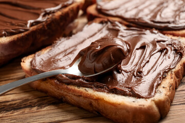 Wooden board of bread with chocolate paste and hazelnuts on table, closeup