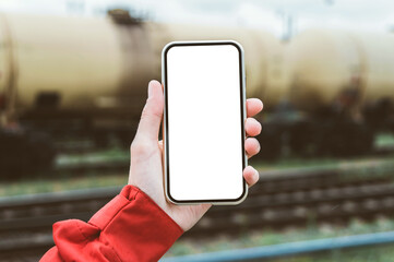 Close-up, smartphone mockup in a man's hand. Against the background of a railway wagon with a tank.