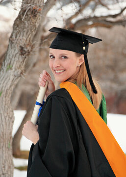 smiling blond woman holding diploma in graduation cap and gown outdoor