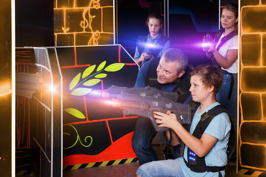 Nice teenager boy and his father aiming laser guns at other players during laser tag game indoors